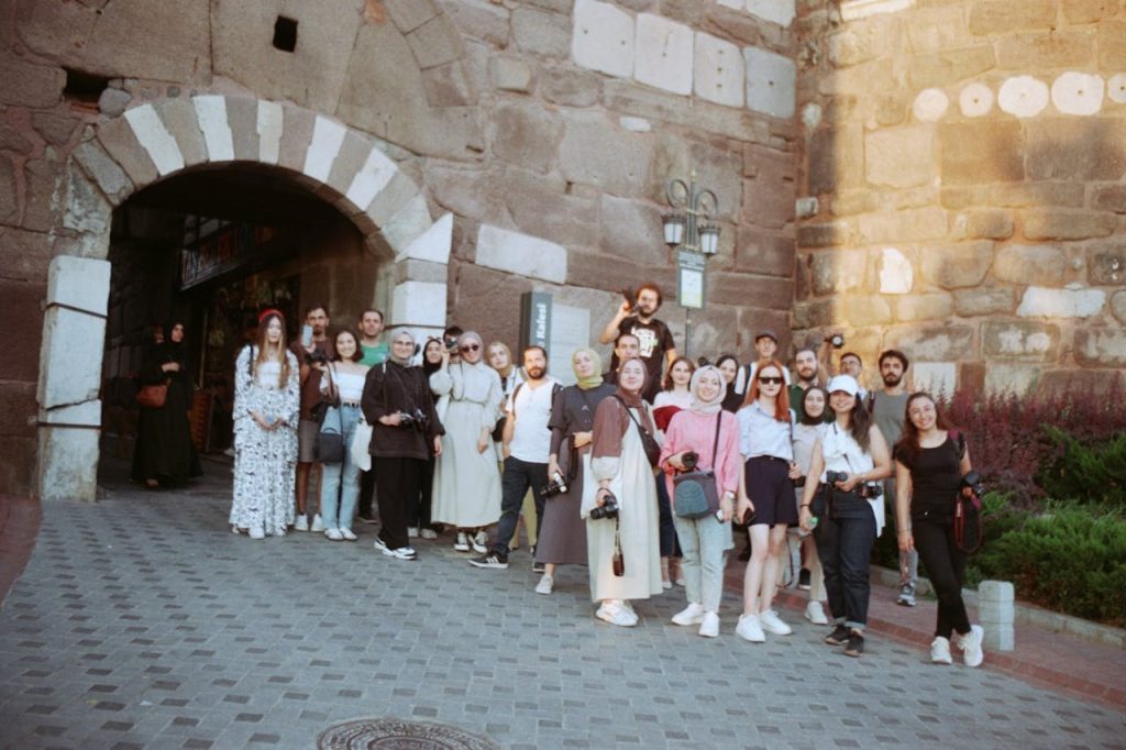 A group of tourists pose at a historic stone city gate, capturing a memorable travel moment.