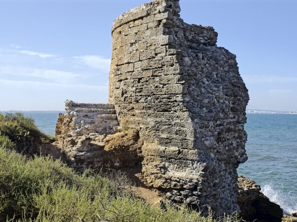 Home Explore the ancient coastal tower ruins in El Puerto de Santa María, Andalucía with a scenic sea backdrop.