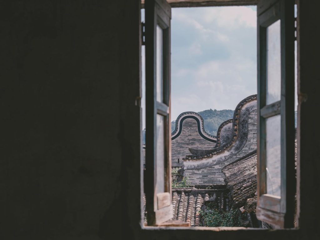 Discover the picturesque view of traditional rooftops framed by an open window in a historic Chinese village.